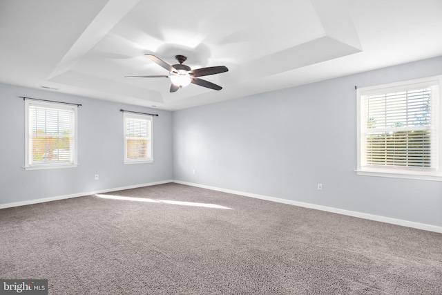 carpeted empty room featuring ceiling fan and a raised ceiling