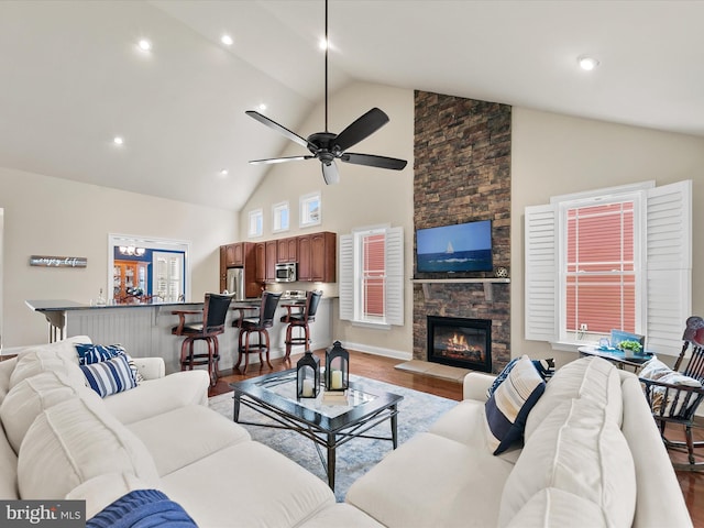 living room with light wood-type flooring, a stone fireplace, ceiling fan, and high vaulted ceiling