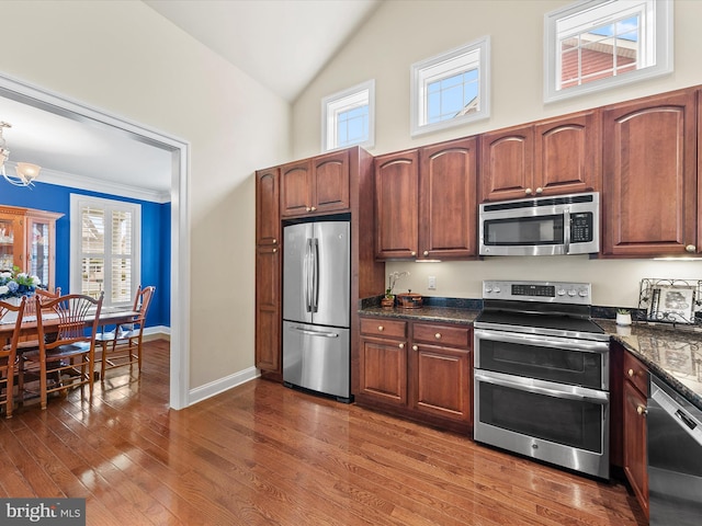 kitchen featuring dark wood-type flooring, stainless steel appliances, a notable chandelier, dark stone counters, and crown molding