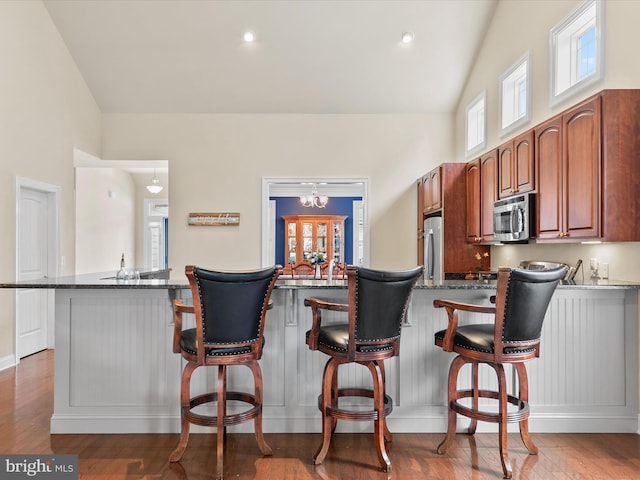 kitchen with dark stone counters, wood-type flooring, a breakfast bar area, lofted ceiling, and stainless steel appliances