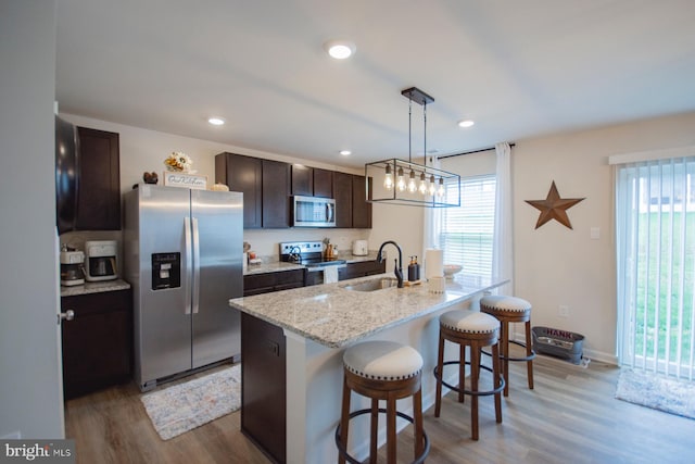 kitchen with stainless steel appliances, light hardwood / wood-style flooring, decorative light fixtures, a center island with sink, and sink