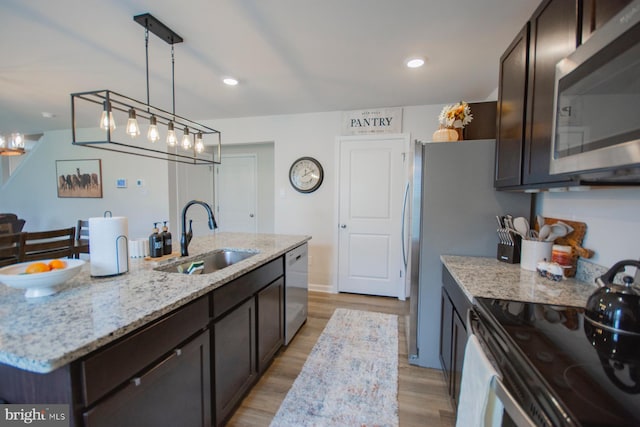 kitchen featuring pendant lighting, an island with sink, sink, light hardwood / wood-style flooring, and appliances with stainless steel finishes