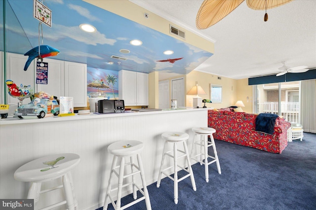 kitchen featuring dark carpet, ceiling fan, kitchen peninsula, white cabinetry, and a breakfast bar area