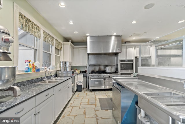 kitchen with wall chimney exhaust hood, white cabinets, stainless steel appliances, and sink