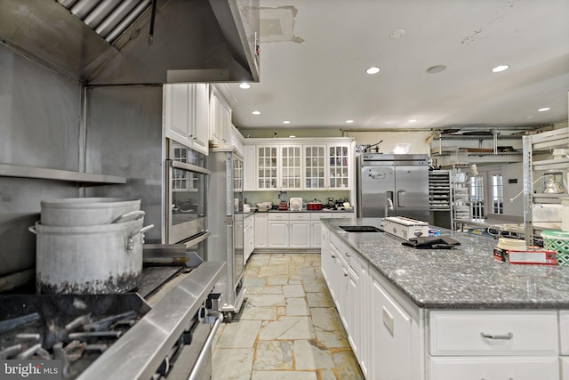 kitchen featuring sink, white cabinetry, stainless steel appliances, custom range hood, and dark stone countertops