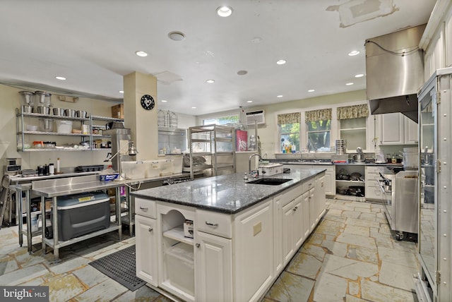 kitchen featuring an island with sink, white cabinets, dark stone counters, and sink