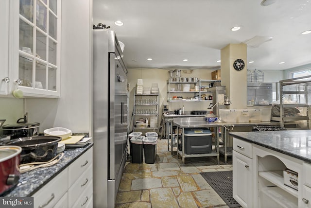 kitchen with dark stone counters, high quality fridge, and white cabinetry