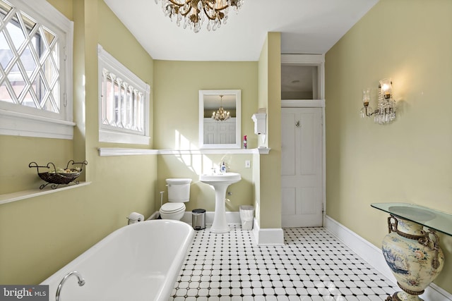 bathroom featuring an inviting chandelier, toilet, a tub, and sink