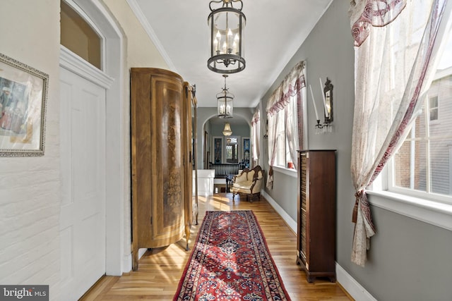 hallway featuring ornamental molding, light hardwood / wood-style flooring, and a notable chandelier