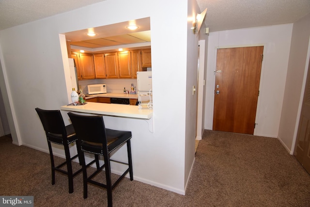 kitchen featuring a textured ceiling, carpet flooring, white appliances, and a breakfast bar