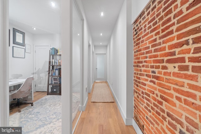 corridor with light hardwood / wood-style flooring and brick wall