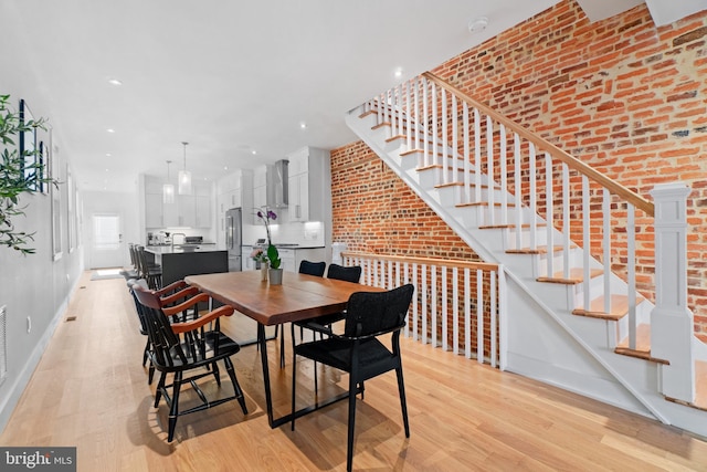 dining area with brick wall and light hardwood / wood-style flooring