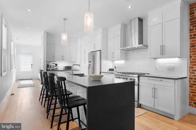 kitchen featuring high end appliances, an island with sink, wall chimney range hood, and light wood-type flooring