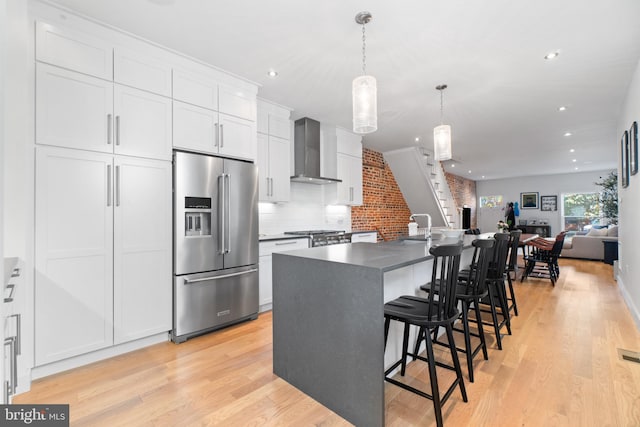 kitchen with wall chimney range hood, a kitchen bar, white cabinetry, stainless steel appliances, and a center island with sink