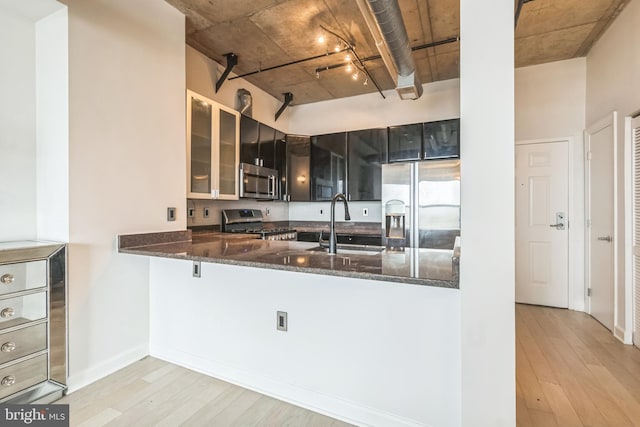 kitchen featuring appliances with stainless steel finishes, kitchen peninsula, dark stone counters, and light wood-type flooring