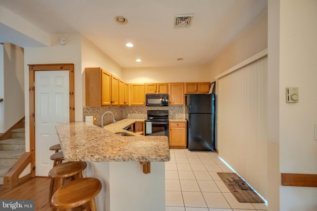 kitchen with black appliances, a kitchen breakfast bar, sink, tasteful backsplash, and kitchen peninsula