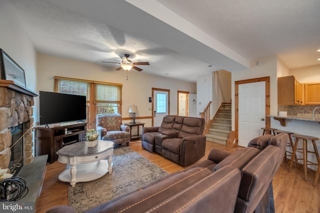 living room featuring light hardwood / wood-style floors, a stone fireplace, and ceiling fan