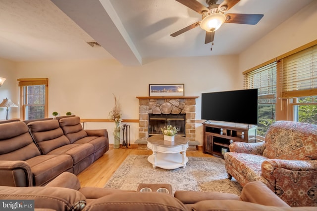 living room featuring beam ceiling, a fireplace, ceiling fan, and light hardwood / wood-style flooring