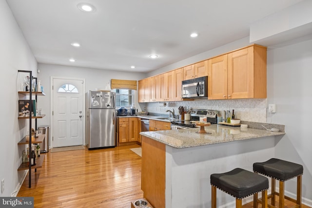 kitchen with stainless steel appliances, light hardwood / wood-style floors, kitchen peninsula, and light stone counters