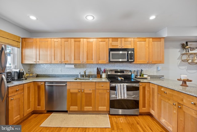 kitchen featuring light hardwood / wood-style flooring, stainless steel appliances, light stone countertops, and sink