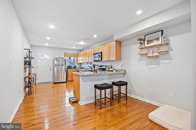 kitchen featuring light brown cabinets, kitchen peninsula, stainless steel appliances, a kitchen breakfast bar, and light wood-type flooring