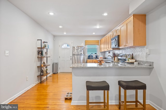 kitchen with kitchen peninsula, light hardwood / wood-style flooring, stainless steel appliances, light brown cabinets, and light stone countertops