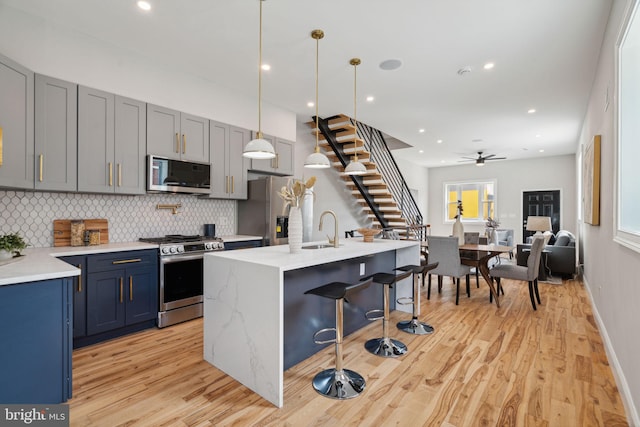 kitchen with ceiling fan, light hardwood / wood-style flooring, a center island with sink, and appliances with stainless steel finishes