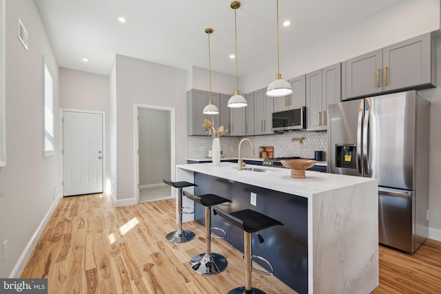 kitchen featuring light stone countertops, appliances with stainless steel finishes, a kitchen bar, light hardwood / wood-style flooring, and gray cabinets