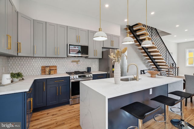 kitchen featuring a kitchen island with sink, sink, light wood-type flooring, appliances with stainless steel finishes, and light stone counters