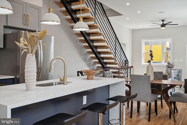 interior space featuring gray cabinetry, sink, light stone counters, light hardwood / wood-style floors, and decorative light fixtures