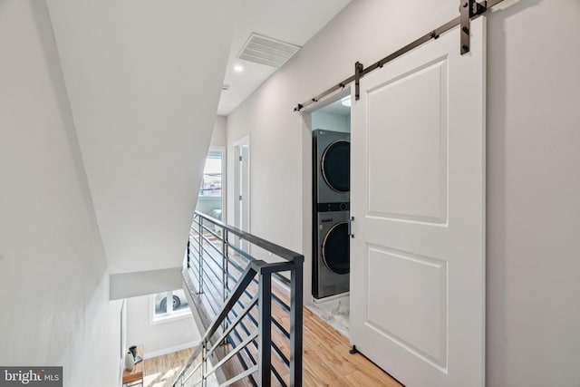 clothes washing area with a barn door, light hardwood / wood-style floors, a wealth of natural light, and stacked washer and clothes dryer