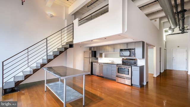 kitchen featuring dark wood-type flooring, stainless steel appliances, a towering ceiling, and beam ceiling