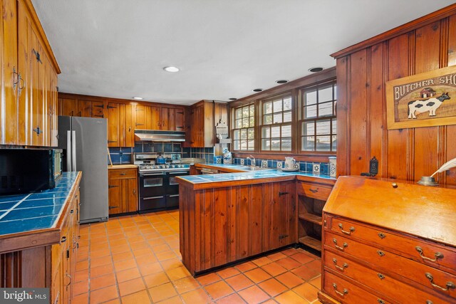 kitchen featuring sink, light tile patterned floors, appliances with stainless steel finishes, tile countertops, and decorative backsplash