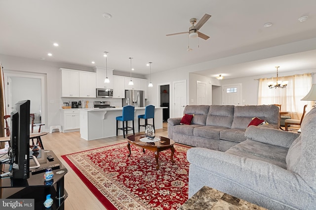 living room with ceiling fan with notable chandelier and light hardwood / wood-style floors