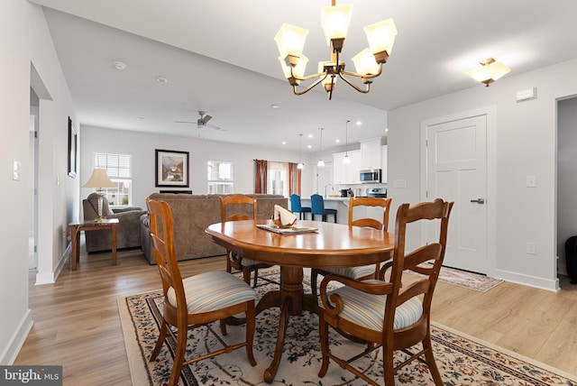 dining space with ceiling fan with notable chandelier and light hardwood / wood-style flooring