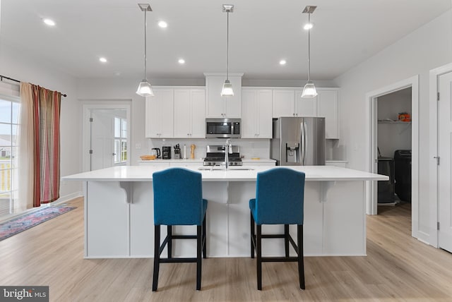 kitchen featuring white cabinets, appliances with stainless steel finishes, a kitchen bar, an island with sink, and sink