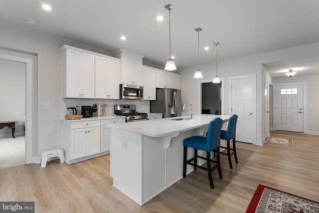 kitchen featuring pendant lighting, white cabinets, appliances with stainless steel finishes, sink, and a kitchen island with sink