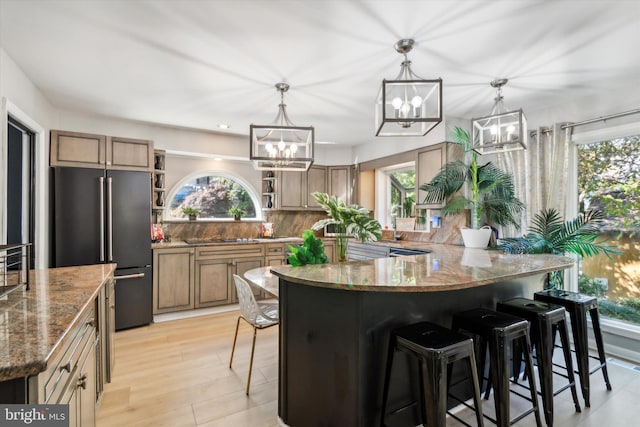 kitchen featuring backsplash, stainless steel fridge, decorative light fixtures, light wood-type flooring, and light stone counters