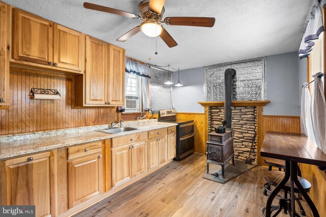 kitchen with ceiling fan, wood walls, a wood stove, light hardwood / wood-style flooring, and range with electric cooktop