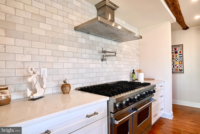 kitchen with light stone counters, double oven range, wall chimney exhaust hood, backsplash, and dark wood-type flooring