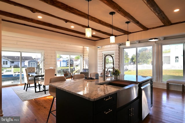 kitchen with hanging light fixtures, a wealth of natural light, light stone countertops, and an island with sink