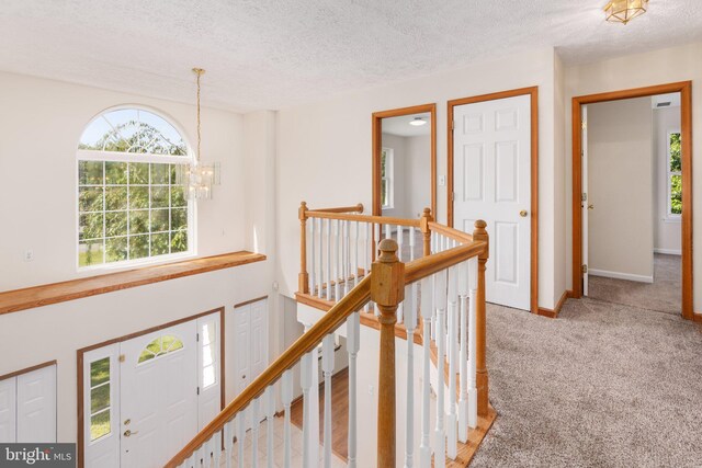 hallway with a chandelier, a textured ceiling, and light colored carpet