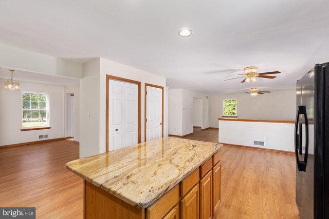 kitchen featuring ceiling fan with notable chandelier, a kitchen island, light hardwood / wood-style flooring, fridge, and light stone countertops