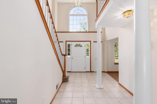 entrance foyer featuring a high ceiling, light tile patterned floors, decorative columns, and a chandelier