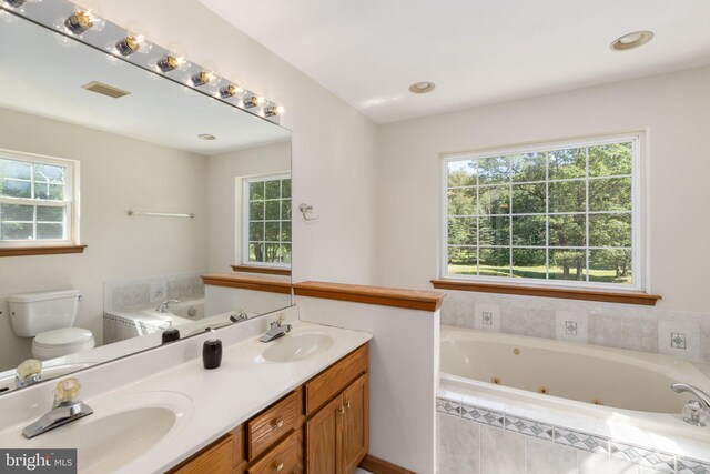 bathroom with a healthy amount of sunlight, tiled tub, and toilet