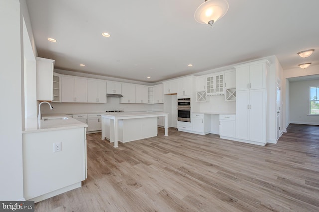 kitchen with a sink, glass insert cabinets, light wood-style floors, and stainless steel double oven