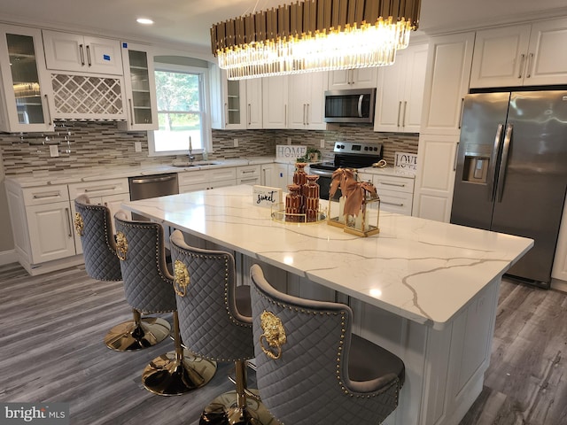 kitchen featuring hardwood / wood-style flooring, a breakfast bar area, white cabinetry, hanging light fixtures, and appliances with stainless steel finishes