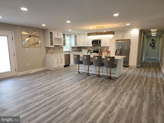 kitchen with pendant lighting, a kitchen island, white cabinetry, appliances with stainless steel finishes, and light wood-type flooring