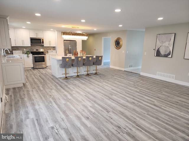 kitchen with light hardwood / wood-style flooring, white cabinets, appliances with stainless steel finishes, and a kitchen island