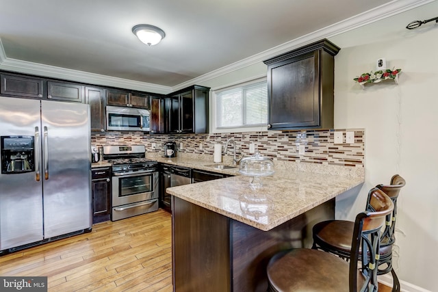 kitchen with light stone counters, light hardwood / wood-style floors, tasteful backsplash, kitchen peninsula, and appliances with stainless steel finishes